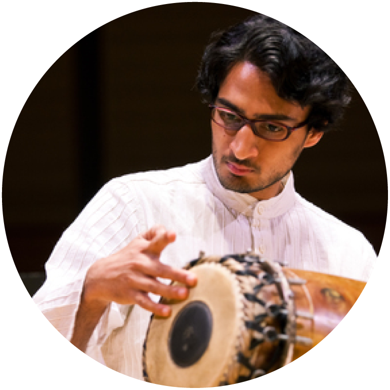Rohan Krishnamurthy wears white and has his right hand on the skin of a mridangam
