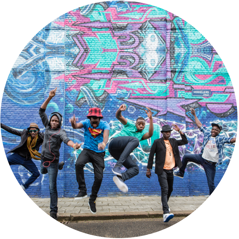 6 members of Mokoomba ecstatically jumping in front of a beautiful pink and blue wall
