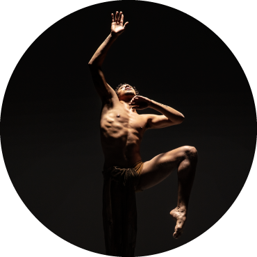 Dancer captured in motion, extending his arm into the air in front of a black backdrop