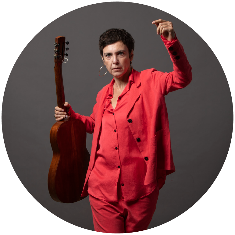 Adrianna Calcanhotto is caught mid dance holding a guitar in an all red suit.