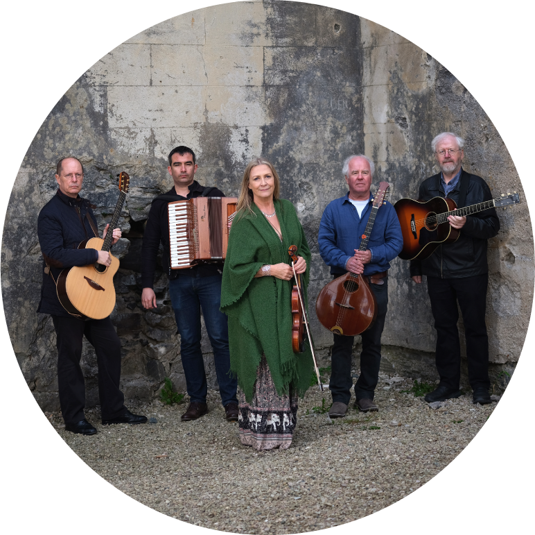 Altan holding their instruments and looking at camera in front of stone wall.