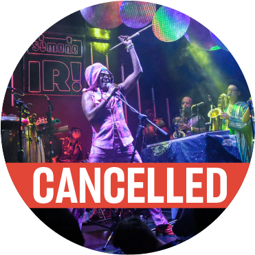 Antibalas performing live. Chinese lanterns hang in the air and the frontman is holding the mic stand in the air. A red colored "cancelled" banner goes across the image.
