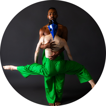 Two dancers pose together wearing green pants against a gray backdrop