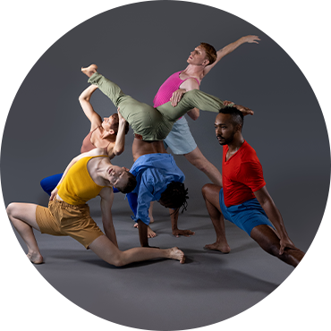 The dancers are captured together in motion wearing multicolored clothing against a gray backdrop