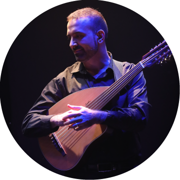 Basel Zayed holds his oud and looks to the side against a black backdrop