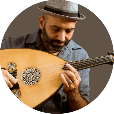 Basel Zayed wears a blue shirt and hat as he plays the oud in front of a gray backdrop