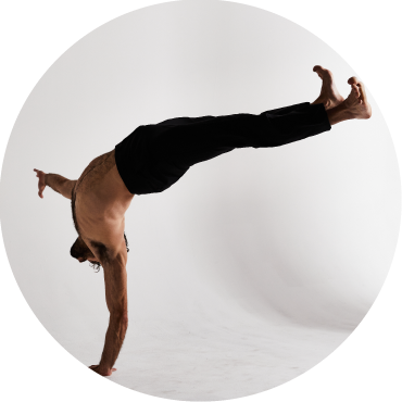 A member of Body Traffic wears black pants and is captured balancing on one hand against a white backdrop