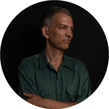 Brad Mehldau looks to the side, wearing a blue shirt against a black backdrop