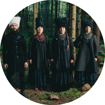 Four members of DakhaBrakha wear black and face forward in front of trees and greenery