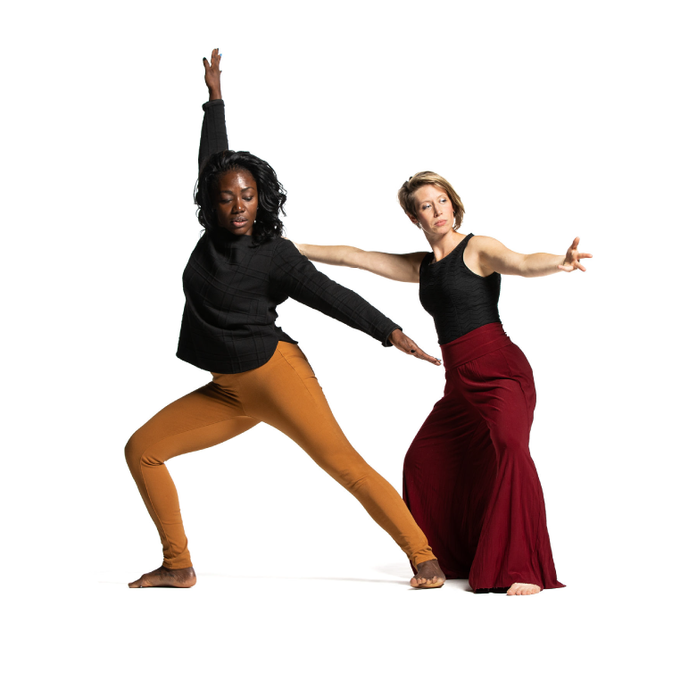 2 dancers, one with dark skin and shoulder-length hair wears a black, long sleeved shirt and yellow pants, raises one arm in the air and the other to their side and stands in a lunge position. The other dancer is light-skinned with short blonde hair, wears a black sleevesless top and baggy red pants and has their arms stretched out to the sides at shoulder length.
