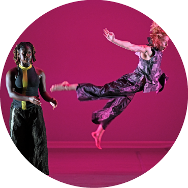 A dancer leaps in the foreground as another dancer stands in the back.