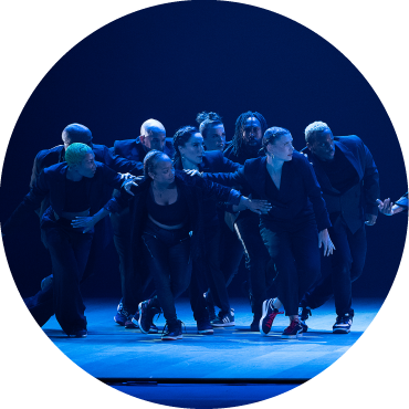 9 Members of Dorrance Dance lightly step very closely together on stage.