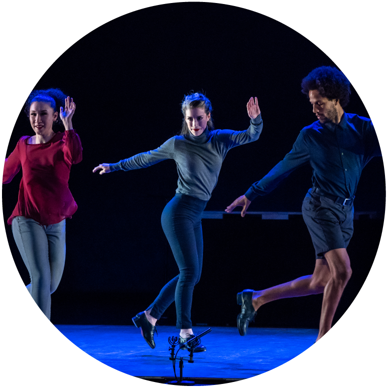 Three dancers all face forward with left legs swinging behind them. 