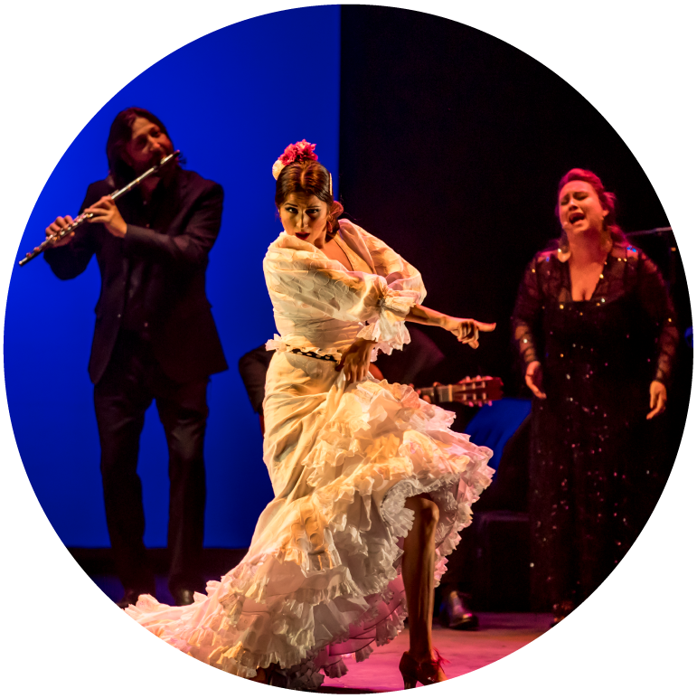 A female dancer is mid dance in a beautiful white dress surrounded by a female singer and a male musician