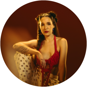 iLE is captured against a brown backdrop wearing a red top and patterned pants
