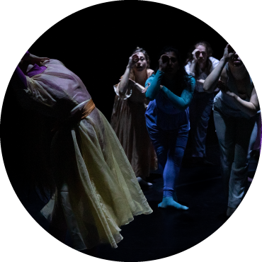 Dancers wear blue and green colored clothing and are captured in motion against a black backdrop