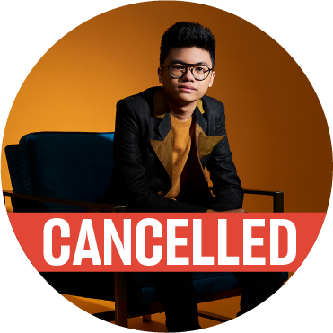 Joey Alexander sits in a black chair with a black denim jacket and yellow lapels against a yellow background with a cancelled banner over the image