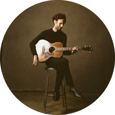 Julian Lage sits on a bench and strums the guitar.