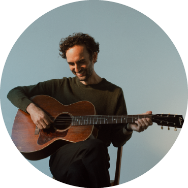 Julian Lage strums the guitar against a blue background.