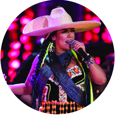 Lila Downs performing live wearing a large hat and colorful outfit