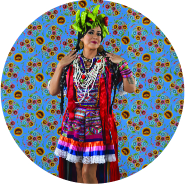 Lila Downs dancing with a crown of peppers on her head against a blue backdrop