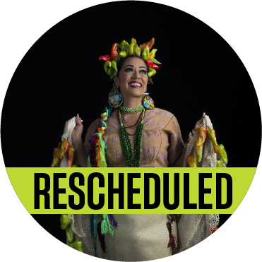 Lila Downs with a crown of peppers on her head with a black background with a banner reading "rescheduled" over the image