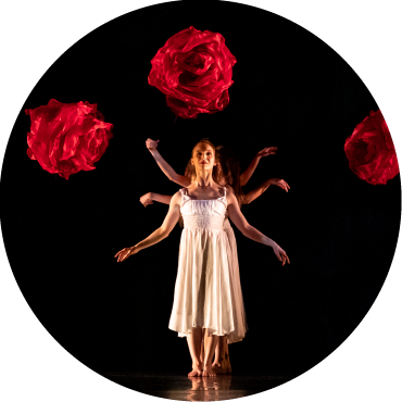 Dancers wear white and stand behind one another with their hands stretched out, against a black and red backdrop