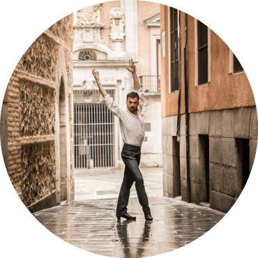 Marco Flores poses with his arms in the air in the alley way of an older looking city.