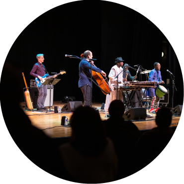 Mike Block and Balla Kouyaté are captured performing live on stage with a band against a black backdrop