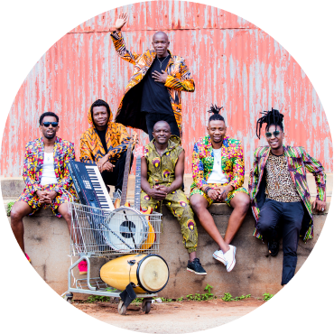 Mokoomba poses together wearing colorful clothing against a bright orange and white backdrop