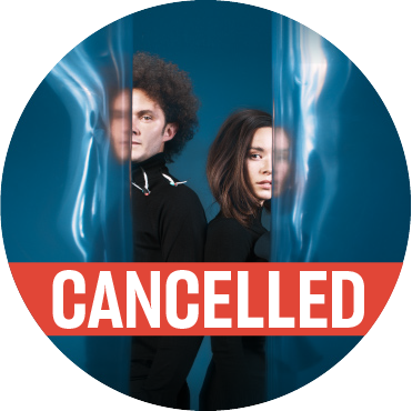A man and a woman, dressed in all black, standing back to back against a blue, water like backdrop with a poppy colored "cancelled" banner going across the image