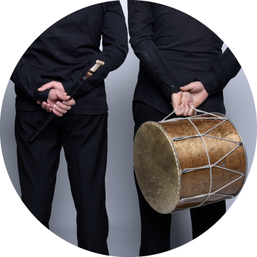 Two people dressed in black hold a drum and a wooden staff behind their backs.