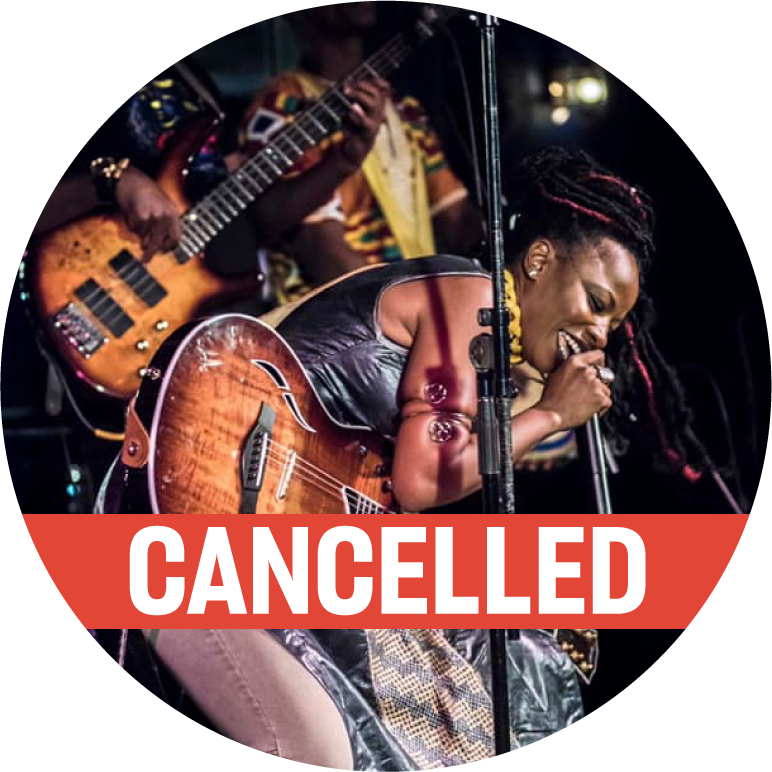 Natu Camara has dark skin with black and red dreadlocks. She wears a black long leather tank top, gray jeans, small stud earrings, and a spiral bracelet on her upper arm. She has a guitar on and bends over and sings into a microphone. There is a red "Cancelled" banner along the bottom.