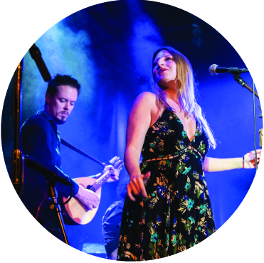 Blonde woman in floral black dance dances in front of man with guitar