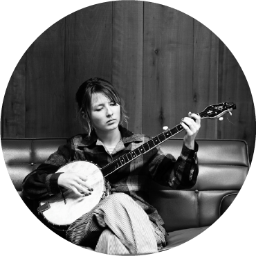Black & White photo of Nora Brown playing the banjo on a sofa.