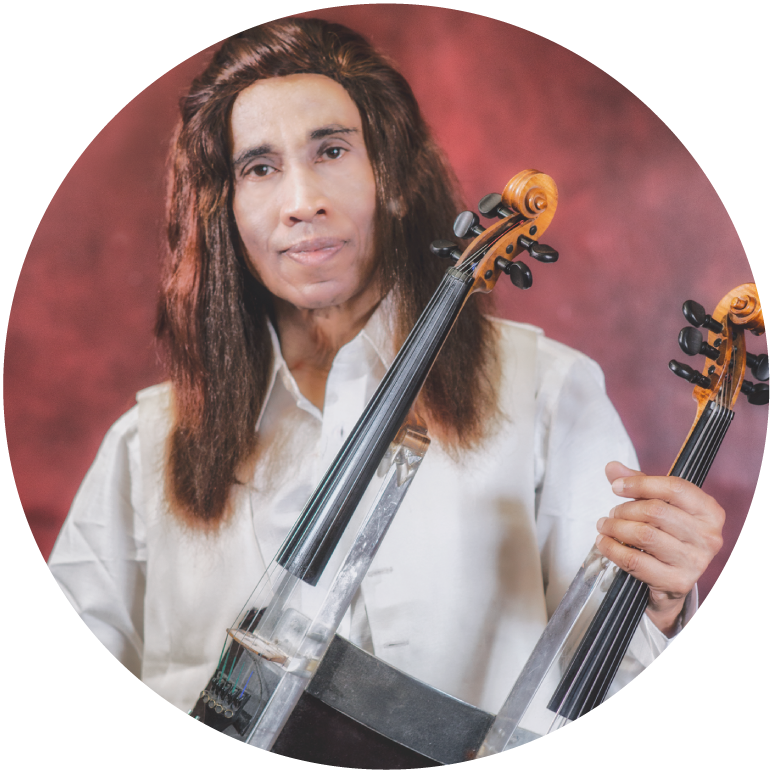 L. Shankar holds a double violin in front of a red background. He has dark skin and red hair that goes past his shoulders. He wears a white shirt.