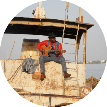 Vieux Farka plays the guitar on top of a boat.