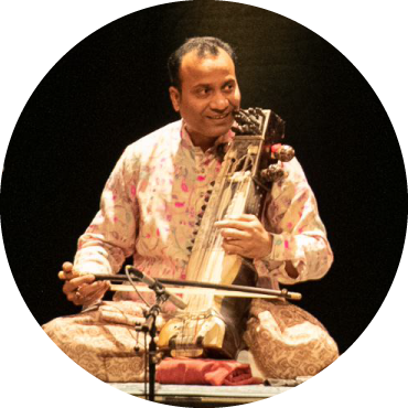 Sabir Khan wears white clothing and plays Sarangi live on stage against a black backdrop