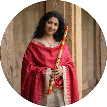 Debopriya Chatterjee wears pink clothing and poses with her flute against a beige backdrop