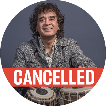 Zakir Hussain wearing a khaki colored top with his hands hovering over the tabla, with a "cancelled" banner over the image