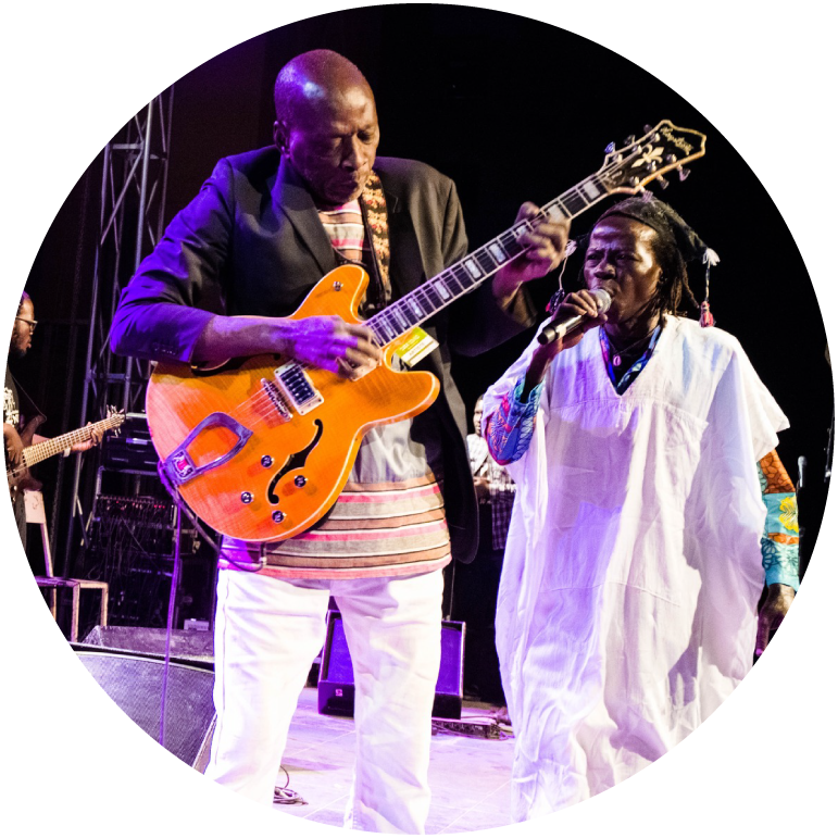 a member of the band performs live on stage with a guitar, while another member wears white and holds a mic