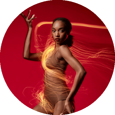 BalletX dancer poses against a red backdrop with one hand up and one on their hip