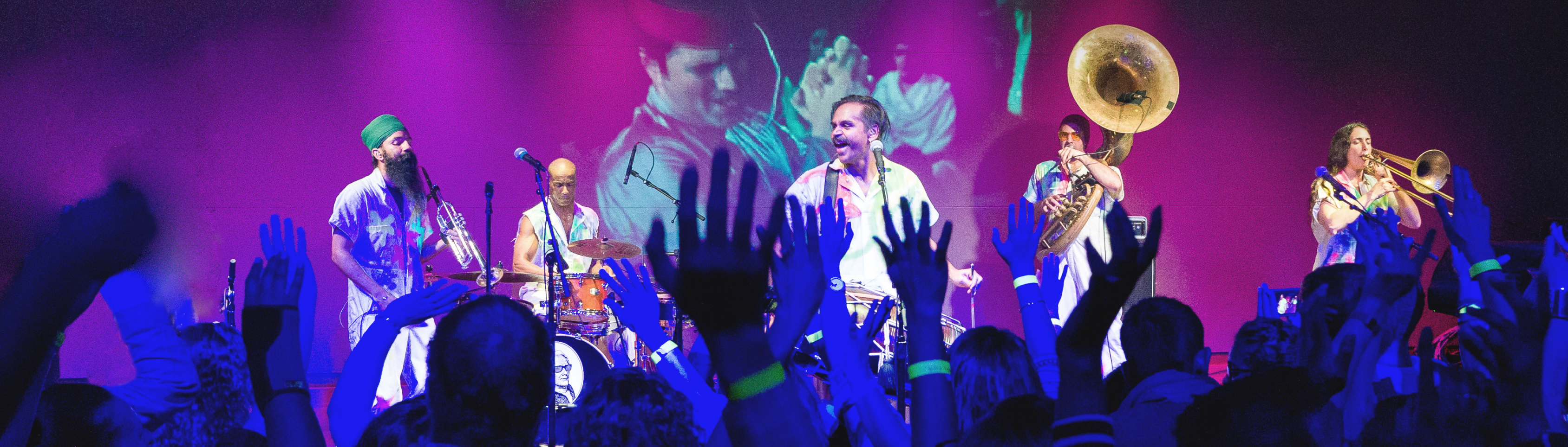 The audience waves their hands in the air as the band Red Baraat performs on stage. The Global Arts Live green logo is on their left