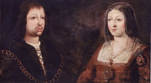 A man and woman sit in front a dark background. Both have light skin and brown hair. The woman is wearing a red dress, a gold necklace, and a crown. The man is wearing a black, gold, and white shirt and has a beard and long hair.