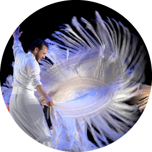 A flamenco dancer wears white and spins a large white scarf against a black background.