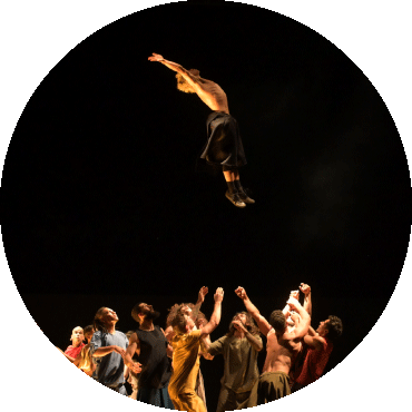 A dancer jumps in the air with a group of dancers below them