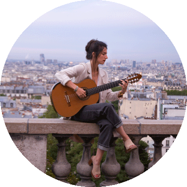 Roxane Elfasci sits on a cement railing while holding a guitar