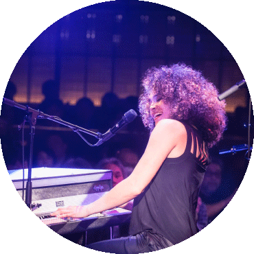 Kandace Springs smiling and playing the piano