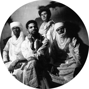 Black and white photo of members of Mdou Moctar pose and wear white clothes and turbans.