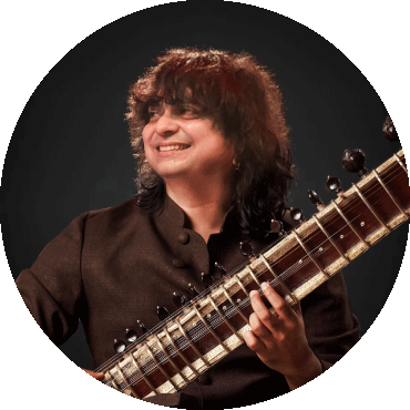 Niladri Kumaar smiles to the side and holds a sitar